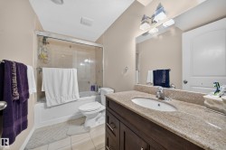 Bathroom featuring a granite-finish vanity with an undermount sink, a dark wood-finish cabinet, and a framed mirror with a contemporary light fixture - 