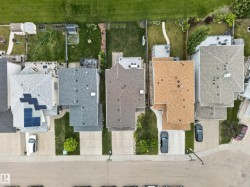 Residential property featuring a grey shingle roof with solar panel installation, concrete driveway, and a front lawn with a single tree - 