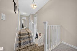 Carpeted staircase with white balusters and newel post, leading to a neutral-toned hallway - 