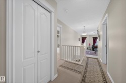 Hallway with neutral wall paint, carpet flooring, white bi-fold closet doors, and white railing - 