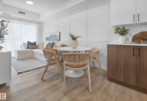 Open-concept living space featuring wood-finish flooring, a contemporary kitchen with wood-tone lower cabinetry and white upper cabinetry, and a living area with a full-height paneled accent wall - 206 860 Secord Boulevard, Edmonton, AB 