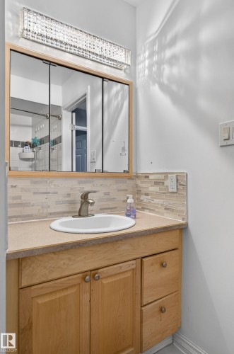 Vanity featuring a light wood-finish cabinet with double doors and two drawers, a rectangular undermount sink, and a brushed nickel faucet - 13445 40 Street Nw, Edmonton, AB 