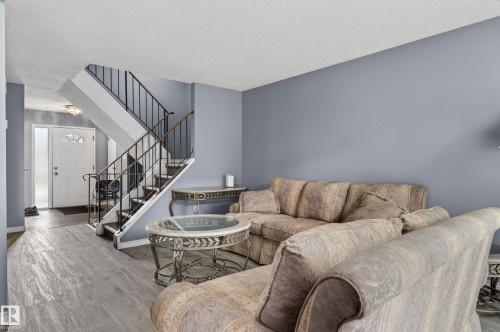 Foyer and living area featuring wood-finish flooring, a white paneled entry door with sidelight, and a staircase with black metal railings - 13445 40 Street Nw, Edmonton, AB 