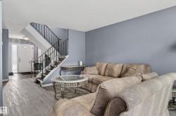 Foyer and living area featuring wood-finish flooring, a white paneled entry door with sidelight, and a staircase with black metal railings - 