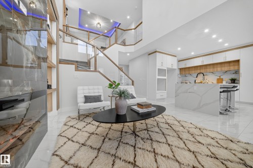 Open-concept living space featuring a contemporary staircase with glass railing, recessed lighting, and a white tile floor - 372 Creekside Green, Leduc, AB 