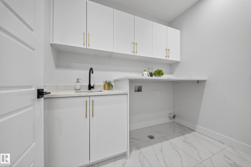 Utility room featuring white cabinetry with gold-tone hardware, a black gooseneck faucet, and an undermount sink - 372 Creekside Green, Leduc, AB 