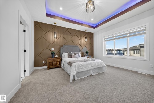 Spacious room featuring a decorative accent wall, tray ceiling with recessed lighting, and large windows - 372 Creekside Green, Leduc, AB 