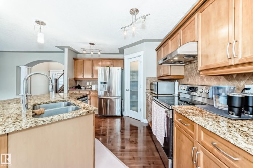 Kitchen featuring wood-finish flooring, light wood cabinetry, stainless steel appliances, granite countertops, and a full-height tile backsplash - 5308 164 Avenue, Edmonton, AB 