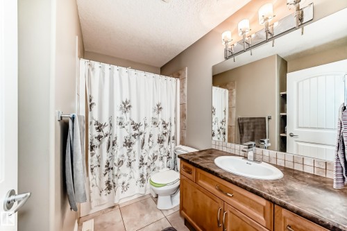 Bathroom featuring a wood-finish vanity with an integrated sink, a tiled backsplash, and an overhead four-light fixture - 5308 164 Avenue, Edmonton, AB 
