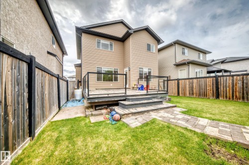 Rear exterior featuring a spacious wooden deck with glass panel railing, a stone paver patio, and a grass lawn - 5308 164 Avenue, Edmonton, AB 