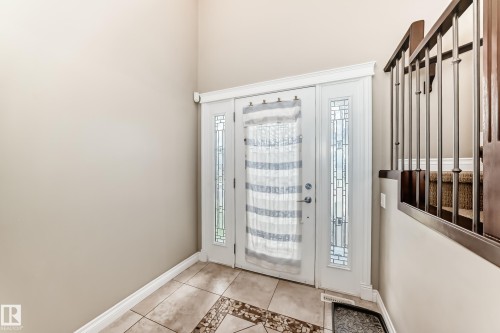 Double entry doors with decorative glass sidelights, ceramic tile flooring, and a carpeted staircase with wrought iron balusters - 5308 164 Avenue, Edmonton, AB 