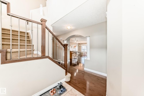Foyer with wood-finish flooring, carpeted staircase with wood handrail and metal spindles, and an arched entryway - 5308 164 Avenue, Edmonton, AB 