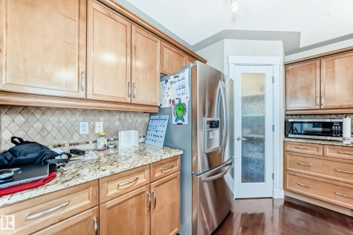 Kitchen featuring wood-finish cabinetry with silver-tone hardware, granite countertops, and a neutral tile backsplash - 5308 164 Avenue, Edmonton, AB 