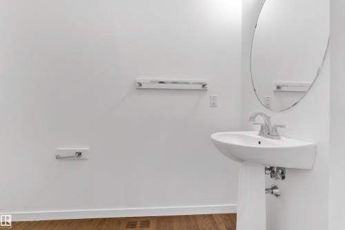 Wall-mounted ceramic sink with chrome faucet, complemented by a round frameless mirror - 5432 20 Avenue, Edmonton, AB 
