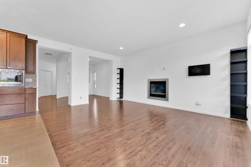 Open-concept living space featuring wood-finish flooring, recessed lighting, and a modern fireplace with a metal surround - 5432 20 Avenue, Edmonton, AB 