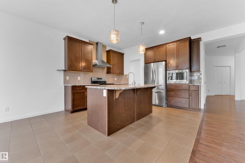 Spacious kitchen featuring dark wood cabinetry, stainless steel appliances, a center island with sink, pendant lighting, and tile flooring - 5432 20 Avenue, Edmonton, AB 