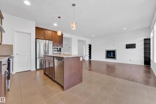 Open-concept living space with a kitchen island, recessed lighting, and a modern fireplace - 5432 20 Avenue, Edmonton, AB 