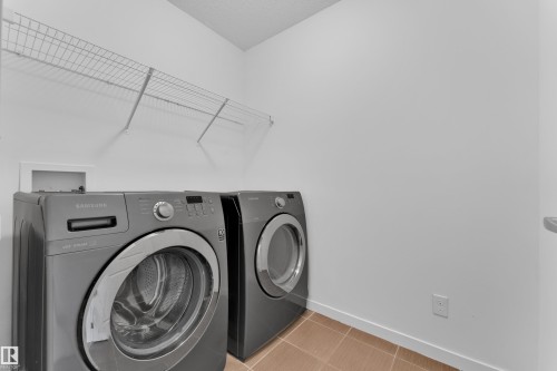 Dedicated utility space featuring a front-loading washer and dryer, wire shelving, light-toned wall paint, and square tile flooring - 5432 20 Avenue, Edmonton, AB 