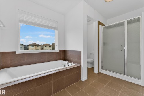 Bathroom featuring a built-in soaking tub with chrome fixtures, a spacious walk-in shower with a frosted glass door, and large format tiled flooring - 5432 20 Avenue, Edmonton, AB 