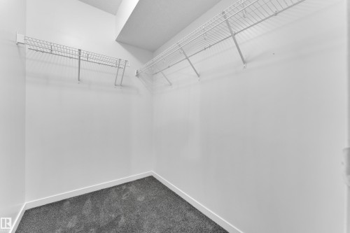 Walk-in closet featuring white wire shelving, white painted walls, and dark grey carpeting - 5432 20 Avenue, Edmonton, AB 