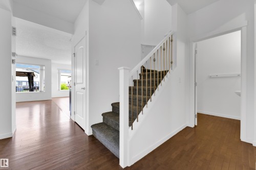 Entryway featuring rich wood-finish flooring, a carpeted staircase with decorative metal spindles, and a white paneled door - 5432 20 Avenue, Edmonton, AB 