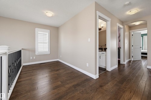 Upper-level hallway featuring wood-finish flooring, neutral wall tones, white baseboards, and a white window with louvered shutters - 21928 97 Avenue, Edmonton, AB 