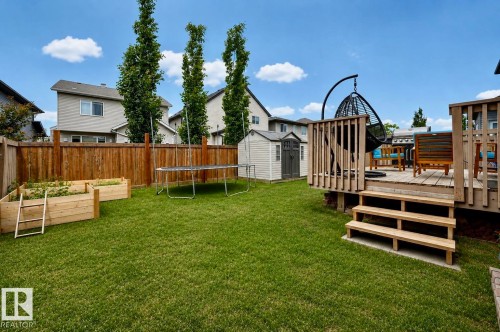 Expansive backyard featuring a wood deck with railings, a manicured lawn, a privacy fence, and two raised garden beds - 21928 97 Avenue, Edmonton, AB 