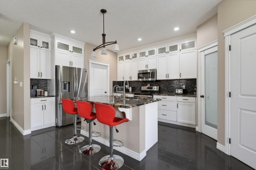 Kitchen featuring a large central island with seating, white cabinetry, dark stone countertops, and stainless steel appliances - 21928 97 Avenue, Edmonton, AB 