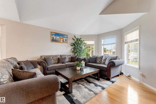 Living area featuring light wood-finish flooring, a recessed vaulted ceiling, and multiple windows with blinds - 4465 32A Street, Edmonton, AB 