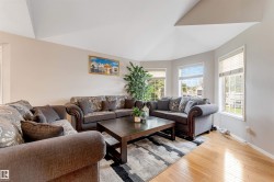 Living area featuring light wood-finish flooring, a recessed vaulted ceiling, and multiple windows with blinds - 