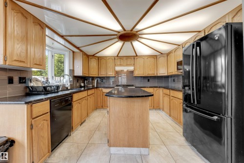 Kitchen featuring light wood cabinetry, dark countertops, tiled backsplash, central island, and tiled flooring - 4465 32A Street, Edmonton, AB 