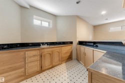Finished lower level space featuring wood cabinetry, dark speckled countertops, a double basin sink, and black and white patterned flooring - 