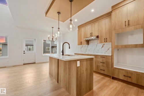 Modern kitchen featuring light wood-finish cabinetry, white countertops, and a full-height marble-look backsplash - 4636 18 Avenue, Edmonton, AB 