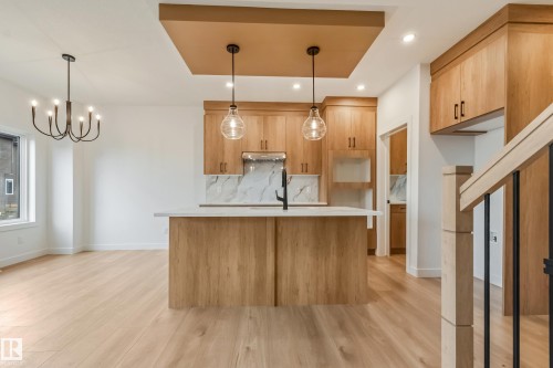 Open-concept kitchen featuring light wood-finish cabinetry, a large kitchen island with a light-toned countertop, and a marble-patterned backsplash - 4636 18 Avenue, Edmonton, AB 