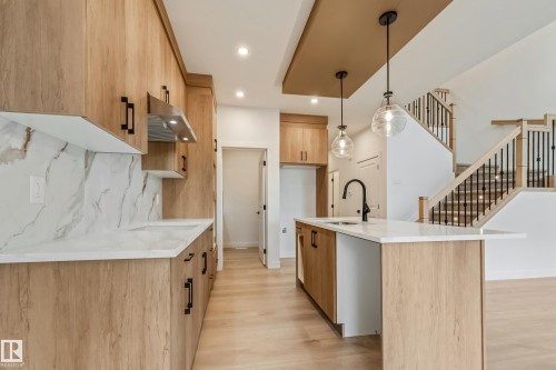 Modern kitchen featuring light wood-finish cabinetry, white countertops with veined backsplashes, a central island with an undermount sink, and black hardware - 4636 18 Avenue, Edmonton, AB 