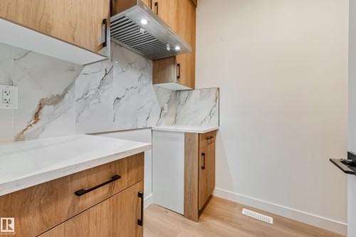 Kitchen area featuring wood-finish cabinetry, white countertops, and a full-height marble-patterned backsplash - 4636 18 Avenue, Edmonton, AB 