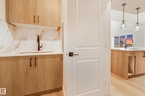 Wet bar featuring light wood-finish cabinetry, a white countertop, and a white and brown veined backsplash - 4636 18 Avenue, Edmonton, AB 