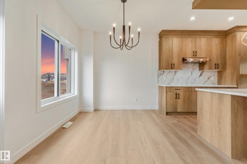 Open-concept kitchen and dining area featuring light wood-finish flooring, a contemporary bronze chandelier, and a large window - 4636 18 Avenue, Edmonton, AB 