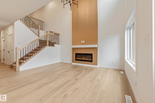 Open-concept living space featuring high ceilings, light wood-finish flooring, and a modern staircase with dark metal spindles and light wood handrails - 4636 18 Avenue, Edmonton, AB 
