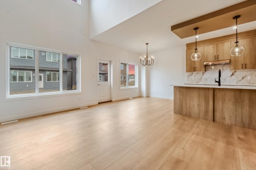 Open-concept living space featuring wood-finish flooring, a kitchen island with pendant lighting, a kitchen with wood-finish cabinetry and a light-toned countertop with a stone-finish backsplash, and tall ceilings - 4636 18 Avenue, Edmonton, AB 