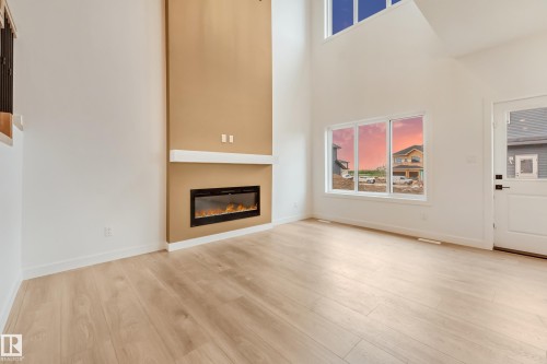 Spacious interior featuring high ceilings, light wood-finish flooring, and a contemporary linear fireplace with a mantle - 4636 18 Avenue, Edmonton, AB 