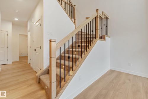 Staircase featuring light wood newel posts and handrails with black metal balusters - 4636 18 Avenue, Edmonton, AB 