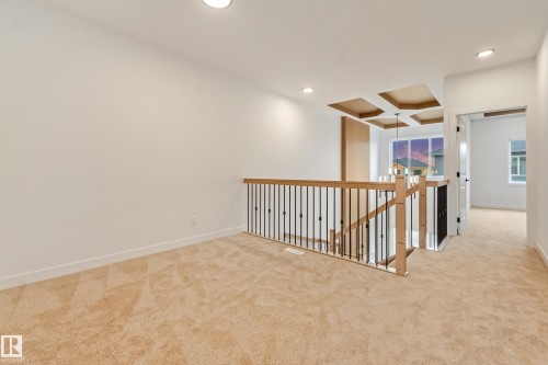 Carpeted upper-level landing featuring a light wood and black metal baluster railing, recessed lighting, and a coffered ceiling detail - 4636 18 Avenue, Edmonton, AB 