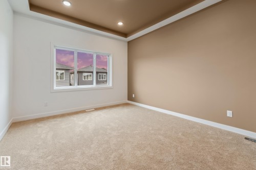 Recessed ceiling lighting illuminating a tray ceiling with a contrasting accent color, neutral carpeting, a large window with white trim, and light beige wall finishes - 4636 18 Avenue, Edmonton, AB 