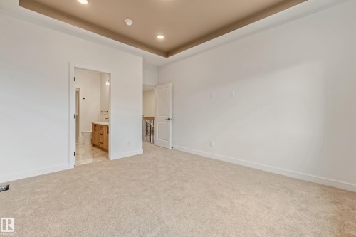 Spacious carpeted room featuring a neutral color palette, a tray ceiling with recessed lighting, and white baseboards - 4636 18 Avenue, Edmonton, AB 