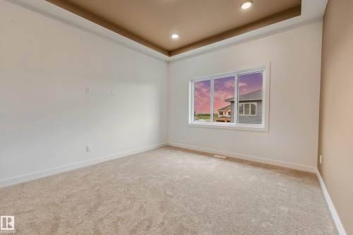 Spacious room featuring neutral carpeting, a large white-framed window, recessed ceiling lighting, and a tray ceiling design with a contrasting accent color - 4636 18 Avenue, Edmonton, AB 