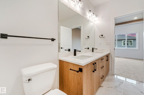 Dual vanity featuring wood-finish cabinetry, white countertops, and matte black fixtures - 4636 18 Avenue, Edmonton, AB 