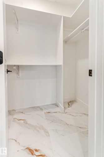 Walk-in closet featuring built-in shelving, hanging rods, and large format white and gold veined tile flooring - 4636 18 Avenue, Edmonton, AB 