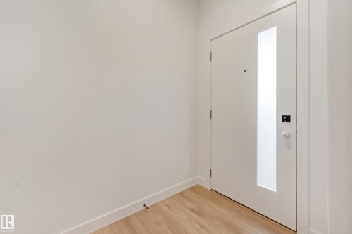 Entry door with a vertical frosted glass panel, contemporary black hardware, light wood-finish flooring, and crisp white baseboards - 4636 18 Avenue, Edmonton, AB 