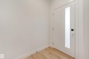 Entry door with a vertical frosted glass panel, contemporary black hardware, light wood-finish flooring, and crisp white baseboards - 4636 18 Avenue, Edmonton, AB 